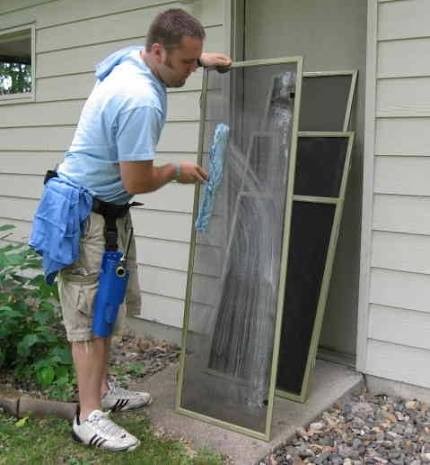 Technician washing a window screen by hand outside an Idaho Falls home
