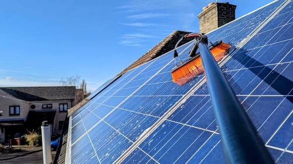 TrueClear cleaning rooftop solar panels with a water-fed pole brush under a blue sky